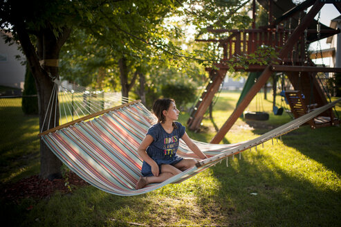 Nachdenkliches Mädchen, das in der Hängematte auf dem Spielplatz sitzt und wegschaut - CAVF60429