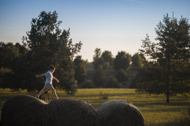 Verspielter Junge läuft auf Heuballen auf einem Feld - CAVF60430