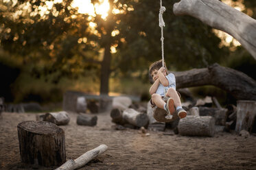 Playful boy swinging on rope swing at park - CAVF60431