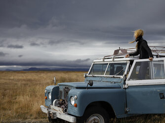 Weibliche Touristin betrachtet die Aussicht, während sie in einem Geländewagen vor stürmischen Wolken steht - CAVF60440