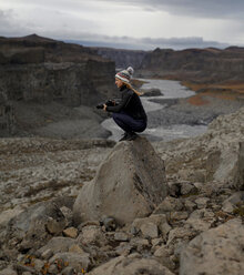 Seitenansicht einer Wanderin, die die Kamera hält, während sie auf einem Felsen hockt - CAVF60441