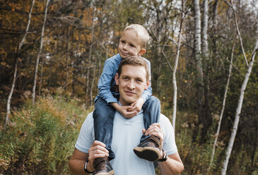 Porträt eines Vaters, der seinen Sohn auf den Schultern trägt, während er im Wald steht - CAVF60446