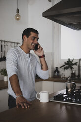 Lächelnder junger Mann am Handy in der Küche zu Hause - ERRF00368