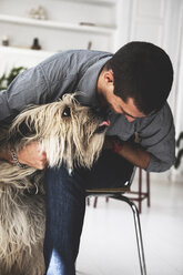 Young man sitting on chair cuddling dog - ERRF00374