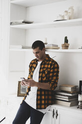 Young man standing at a shelf using cell phone - ERRF00391