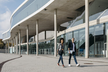 Zwei Kollegen gehen vor einem Bürogebäude spazieren - JRFF02184