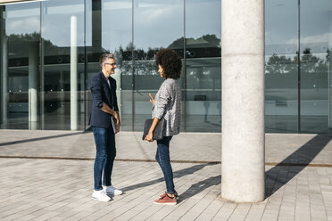 Zwei Kollegen unterhalten sich vor einem Bürogebäude - JRFF02186