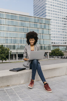 Portrait of smiling businesswoman working with laptop outside office building - JRFF02196