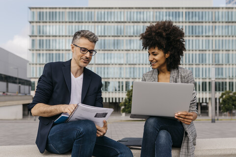 Zwei selbstbewusste Kollegen arbeiten zusammen vor einem Bürogebäude, lizenzfreies Stockfoto