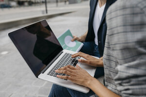 Nahaufnahme von zwei Kollegen, die gemeinsam an einem Laptop im Freien arbeiten - JRFF02202