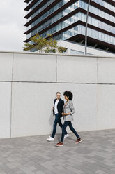 Zwei glückliche Kollegen gehen vor einem Bürogebäude spazieren - JRFF02210