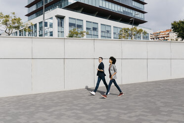 Zwei glückliche Kollegen gehen vor einem Bürogebäude spazieren - JRFF02211