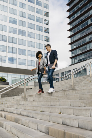 Zwei Kollegen gehen und unterhalten sich auf einer Treppe vor einem Bürogebäude in der Stadt, lizenzfreies Stockfoto