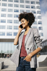 Lächelnde Geschäftsfrau am Mobiltelefon vor einem Bürogebäude - JRFF02230