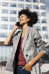 Lachende Geschäftsfrau am Mobiltelefon vor einem Bürogebäude - JRFF02231