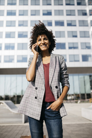 Lächelnde Geschäftsfrau am Mobiltelefon vor einem Bürogebäude, lizenzfreies Stockfoto