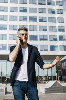 Verärgerter Geschäftsmann mit Mobiltelefon vor einem Bürogebäude - JRFF02235