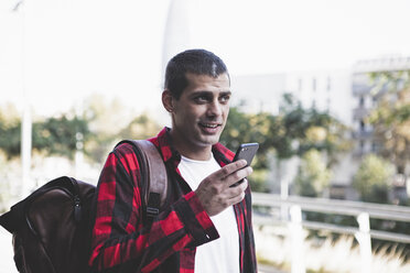 Junger Mann mit Rucksack und Mobiltelefon unterwegs - ERRF00400