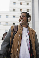 Happy young manwith backpack wearing headphones in the city - ERRF00402