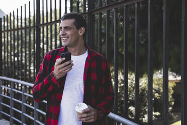 Smiling young man with takeaway coffee and cell phone on the go - ERRF00408