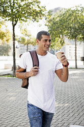 Lächelnder junger Mann mit Kaffee zum Mitnehmen auf dem Weg - ERRF00420