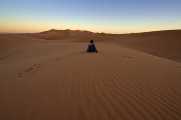 Morocco, back view of woman sitting on desert dune at twilight - EPF00506