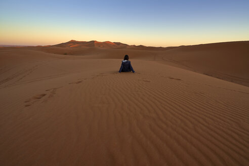 Marokko, Rückenansicht einer auf einer Wüstendüne sitzenden Frau in der Abenddämmerung - EPF00506