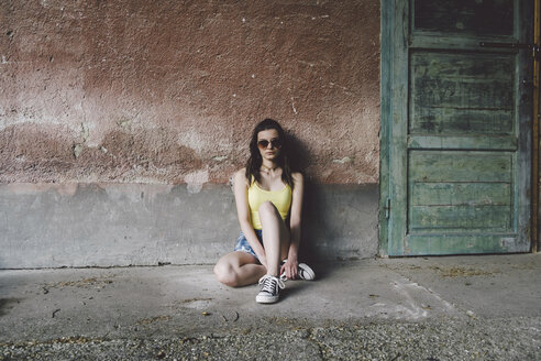 Porträt einer Frau mit Sonnenbrille, die an einer alten Mauer sitzt - CAVF60481