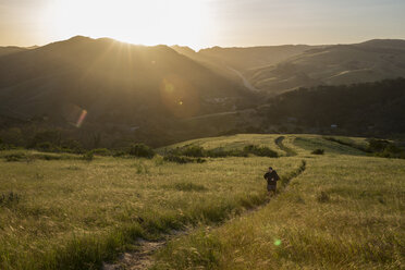 High angle view of man on trail amidst grassy field against mountains during sunset - CAVF60482