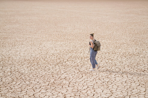 Seitenansicht einer Frau mit Rucksack, die durch eine karge Landschaft läuft - CAVF60494