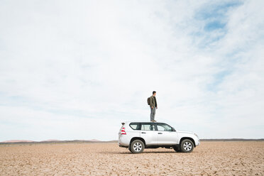 Side view of man standing on off-road vehicle at barren landscape against cloudy sky - CAVF60498