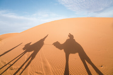 Shadow of friends riding camels on sand at Merzouga desert against sky - CAVF60503