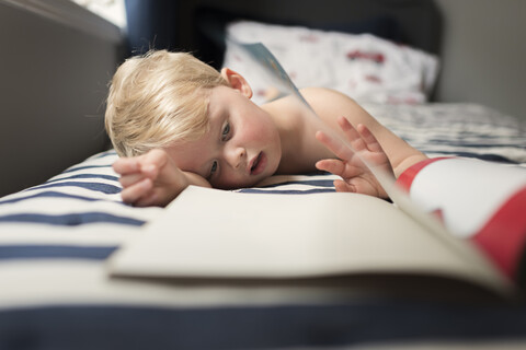 Junge liest Bilderbuch, während er zu Hause auf dem Bett liegt, lizenzfreies Stockfoto