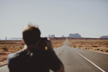 Rückansicht eines Wanderers, der die Landschaft auf einer Landstraße gegen den klaren Himmel fotografiert - CAVF60538
