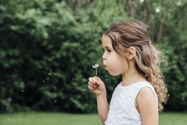 Close-up of girl blowing dandelion while standing on field - CAVF60542