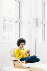 Businesswoman using smart phone while sitting on chair in office - CAVF60566