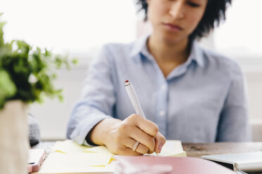 Geschäftsfrau schreibt auf Haftnotiz bei der Arbeit am Schreibtisch im Büro - CAVF60575