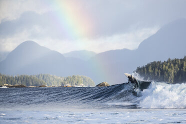 Rückansicht eines Mannes, der auf Wellen im Meer surft, gegen einen Regenbogen - CAVF60585