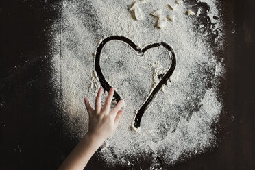 Cropped hand of girl making heart shape of flour on table - CAVF60612