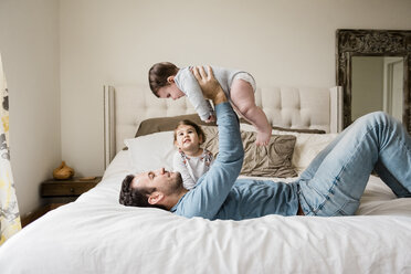 Playful father lifting son while lying by daughter on bed at home - CAVF60623