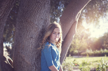 Porträt eines selbstbewussten Mädchens, das im Park Kaugummi gegen einen Baumstamm bläst - CAVF60629