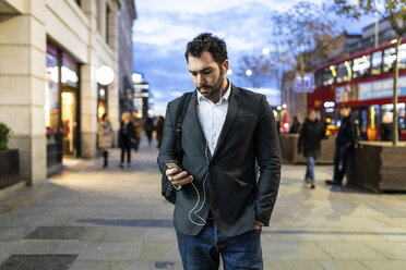 UK, London, businessman on the go checking his phone while commuting by night - WPEF01184