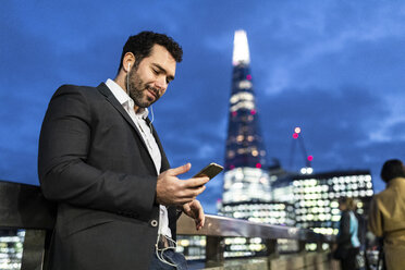 UK, London, businessman on the go checking his phone while commuting by night - WPEF01185