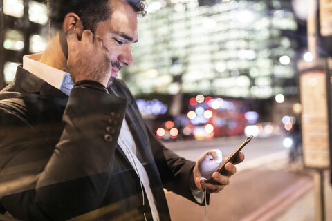 UK, London, Geschäftsmann, der nachts auf dem Weg zur Arbeit sein Telefon überprüft, lizenzfreies Stockfoto