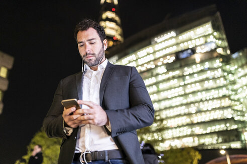 UK, London, Geschäftsmann, der nachts auf dem Weg zur Arbeit sein Telefon überprüft - WPEF01197