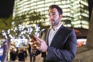 UK, London, Geschäftsmann unterwegs mit Handy in der Hand bei nächtlichem Pendeln - WPEF01199