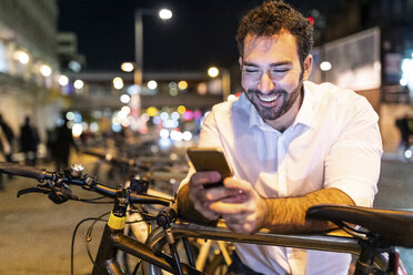 UK, London, glücklicher Mann, der bei Nacht auf sein Telefon schaut - WPEF01203
