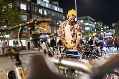 UK, London, Mann schließt sein Fahrrad auf und fährt nachts in der Stadt, lizenzfreies Stockfoto