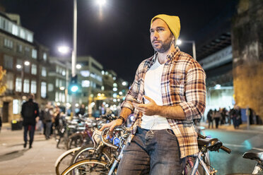 UK, London, Mann mit Fahrrad und Handy beim nächtlichen Pendeln in der Stadt - WPEF01208