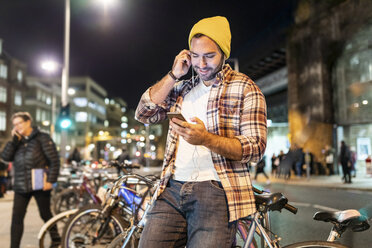 UK, London, Mann pendelt nachts in der Stadt und schaut auf sein Handy - WPEF01209